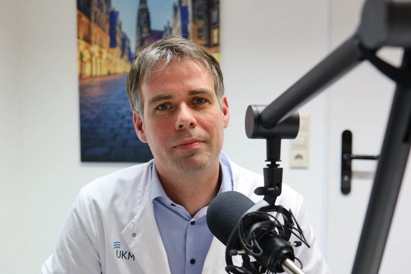 UKM | Arzt im weißen Kittel hinter einem Mikrofon.