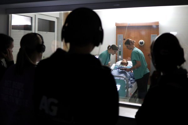 UKM | Zwei Medizinstudentinnen im grünen Kasak sind über einen Patienten gebeugt, der auf einer Liege liegt. Vier Medizinstudierende schauen zu.