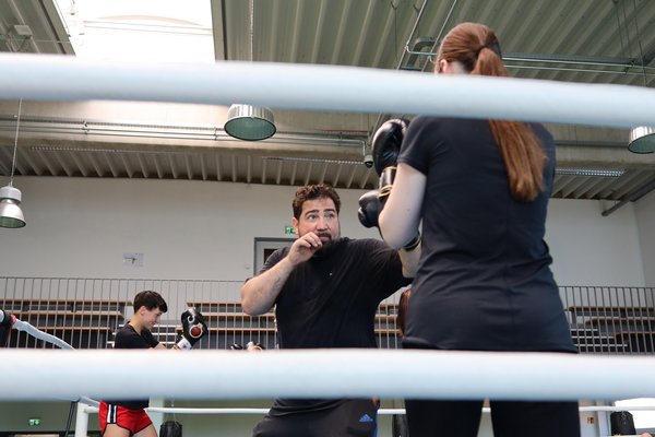 Trainer boxt mit Frau auf einer blauen Matte.