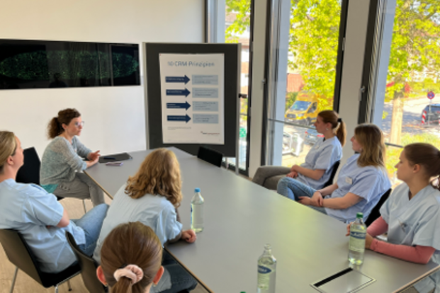 UKM | 7 Personen an einem langen dunklen Tisch bei einer Schulung