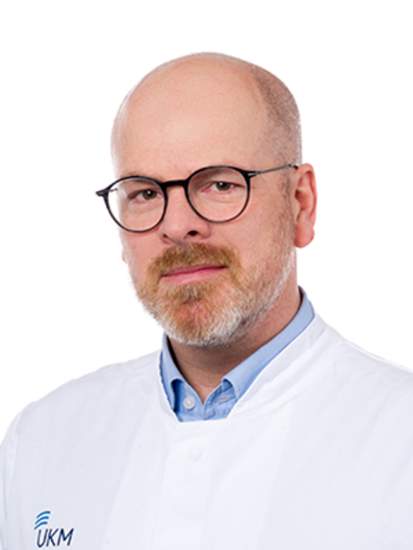 UKM | Portraitaufnahme des Klinikdirektors der Klinik für Unfall-, Hand- und Wiederherstellungschirurgie. Der Arzt trägt einen weißen Kittel, eine Brille und lächelt.