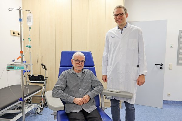UKM | Alzheimerpatient sitzt in blauem Behandlungsstuhl. Arzt in weißem Kittel steht daneben.